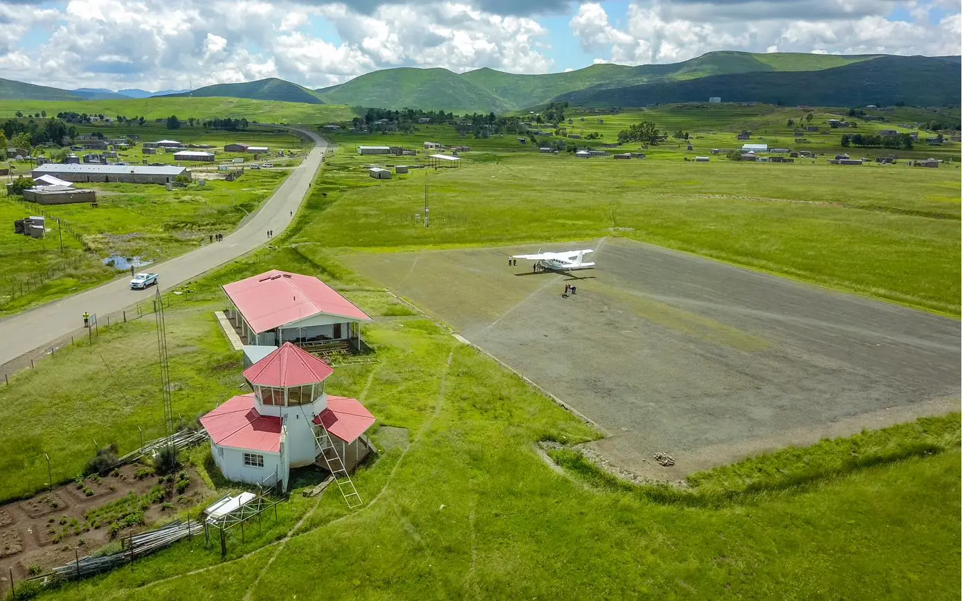 Aerial view of a small Lesotho airfield with a light aircraft on the apron, surrounded by green hills