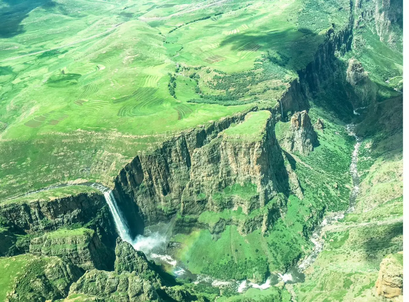 Aerial view of a waterfall dropping from green highland cliffs in Lesotho